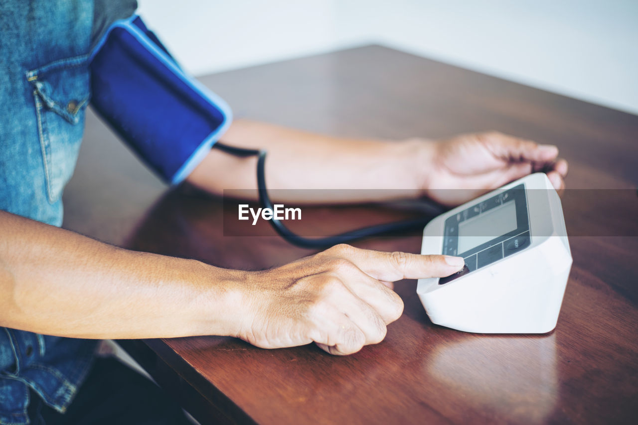 Midsection of woman using blood pressure machine at table