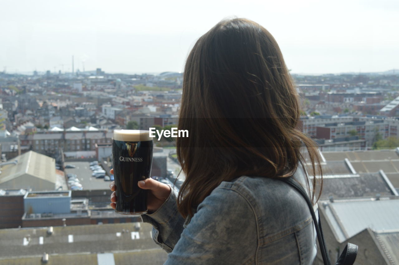 REAR VIEW PORTRAIT OF WOMAN STANDING ON CITYSCAPE