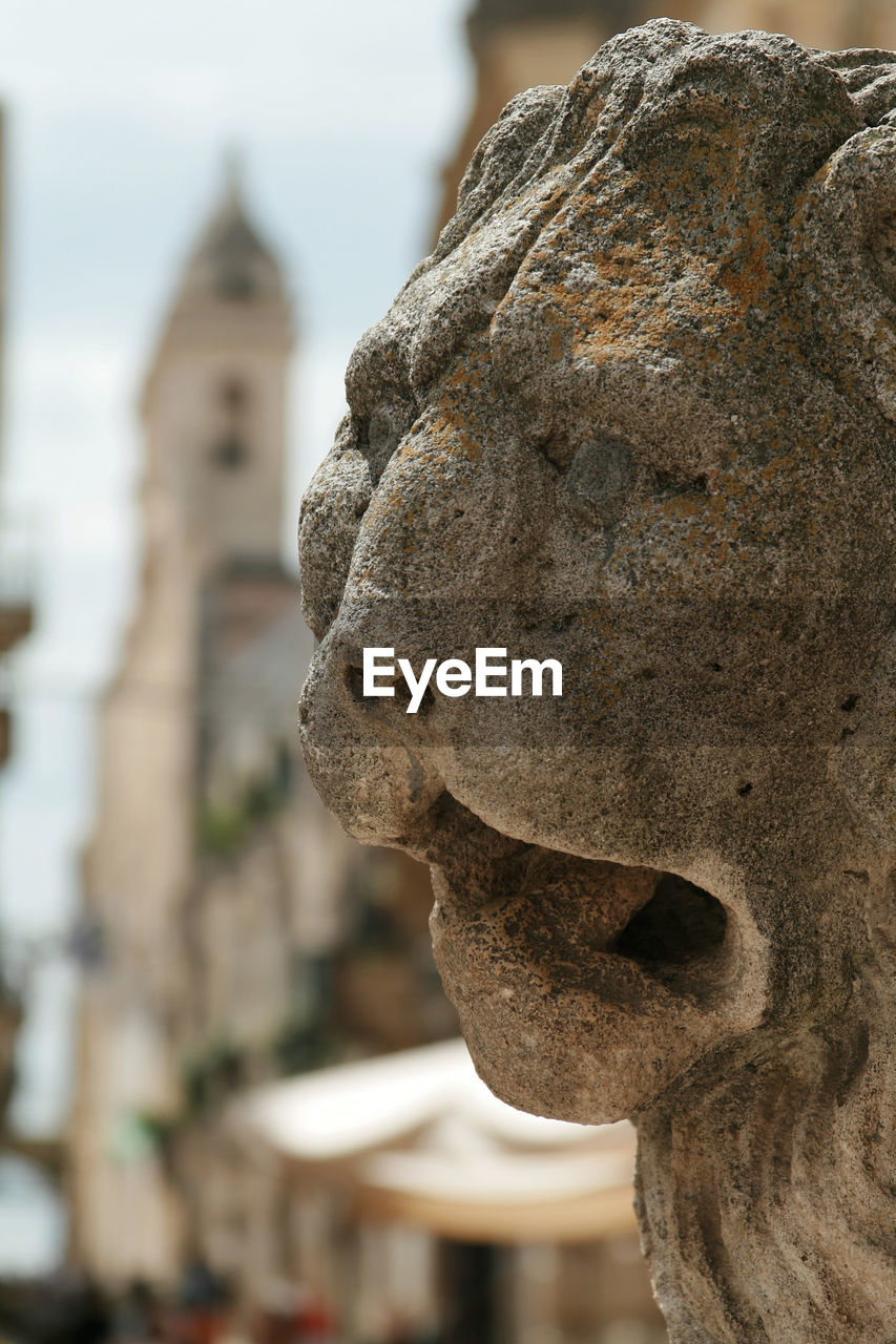 CLOSE-UP OF OLD STATUE AGAINST TEMPLE BUILDING