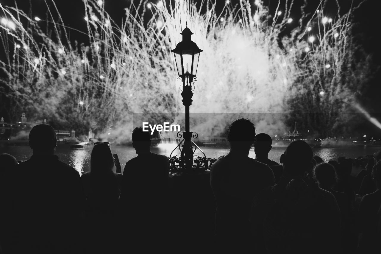 Silhouette people looking at firework display during night