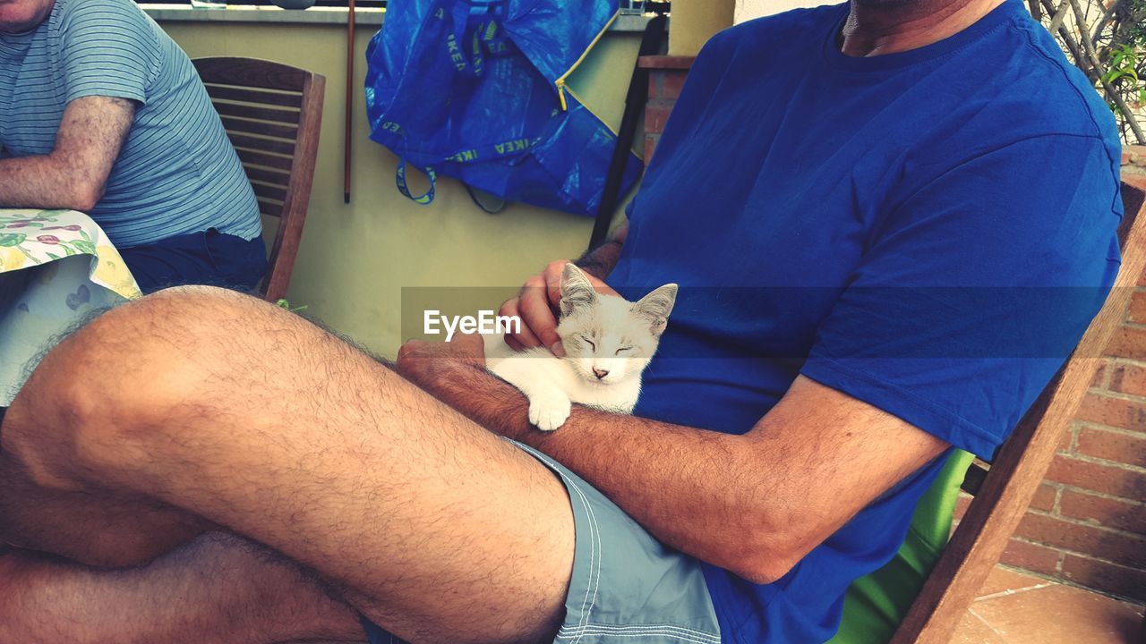 MIDSECTION OF MAN HOLDING DOG SITTING IN BEDROOM