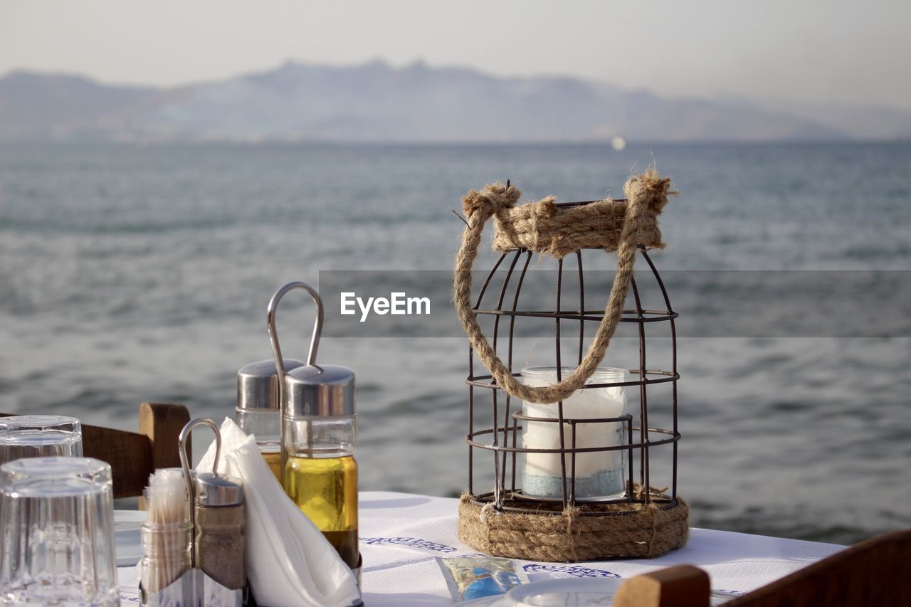 Lantern by olive oil in container on table against sea