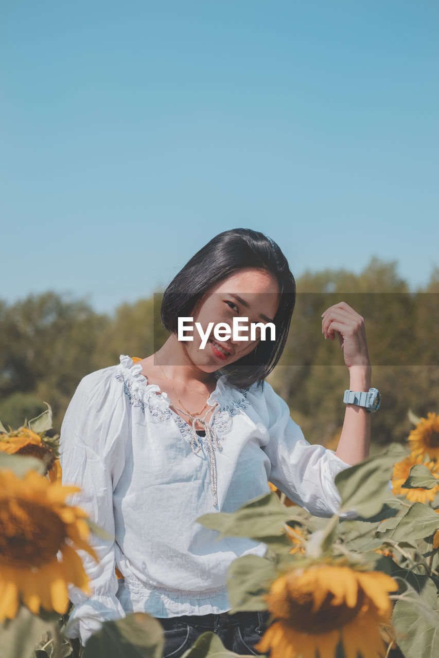 Young woman standing by flowering plants against sky