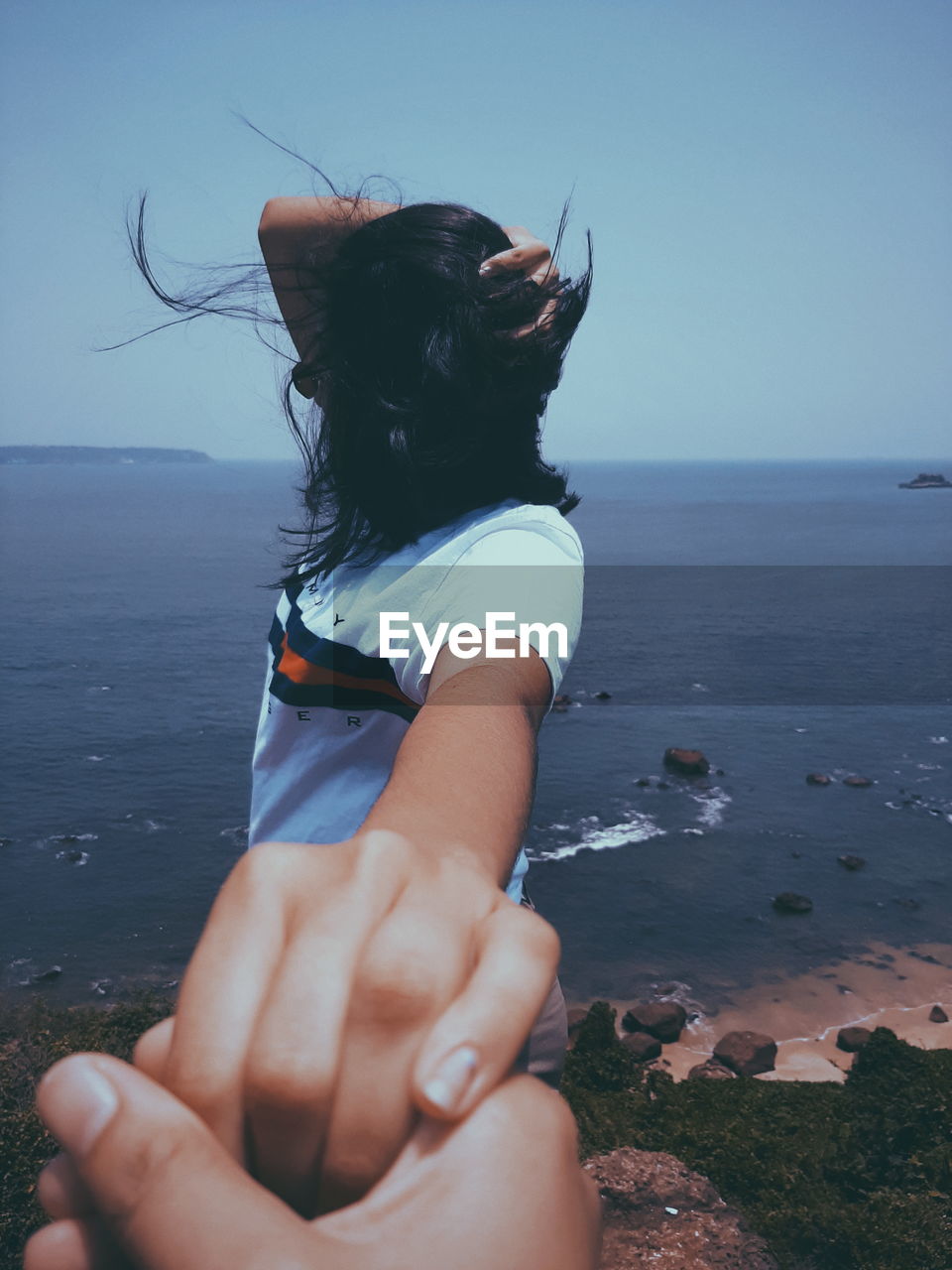 Cropped hand holding hand of woman at beach against clear sky