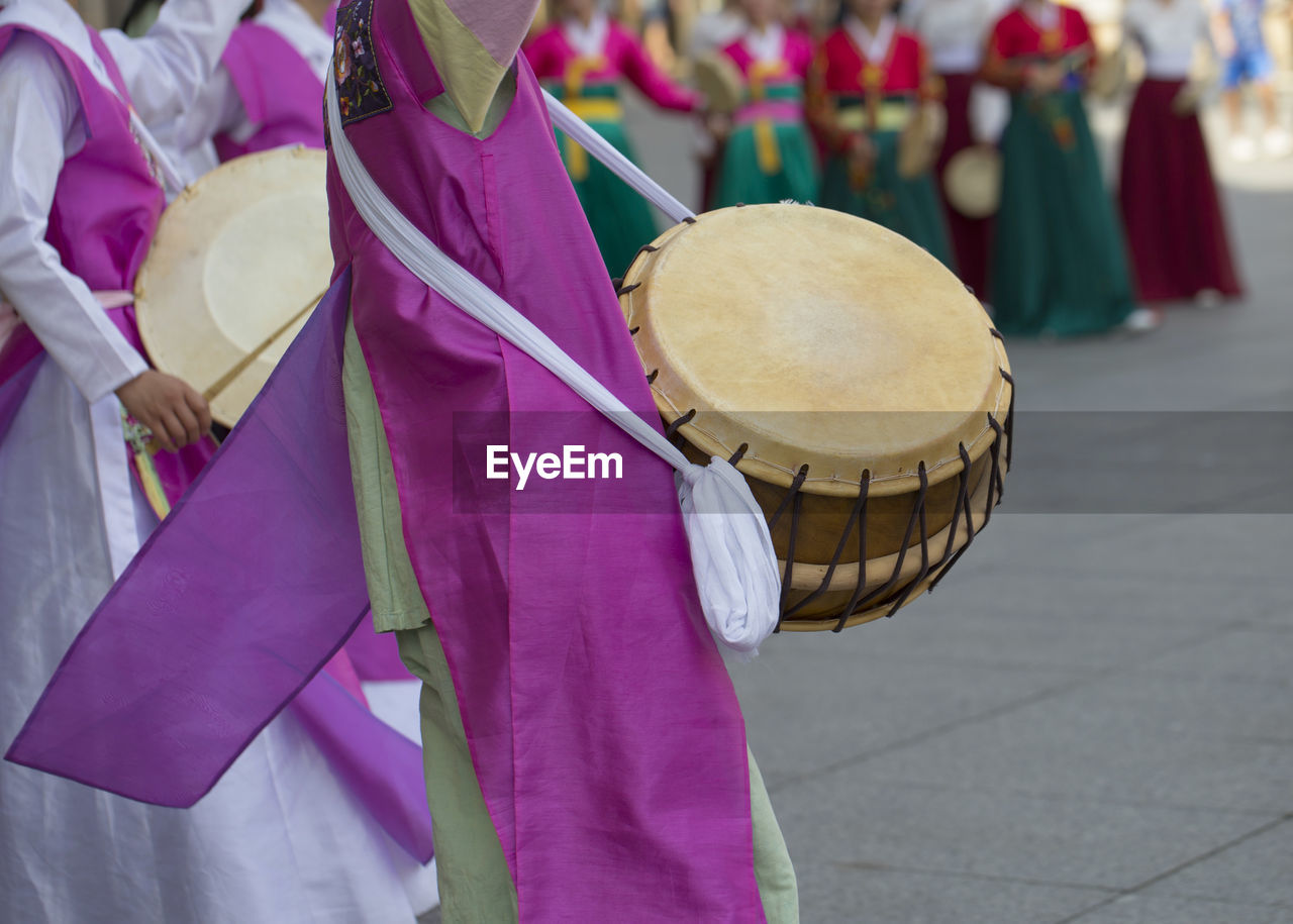 Women in traditional clothing with drums dancing on footpath in city