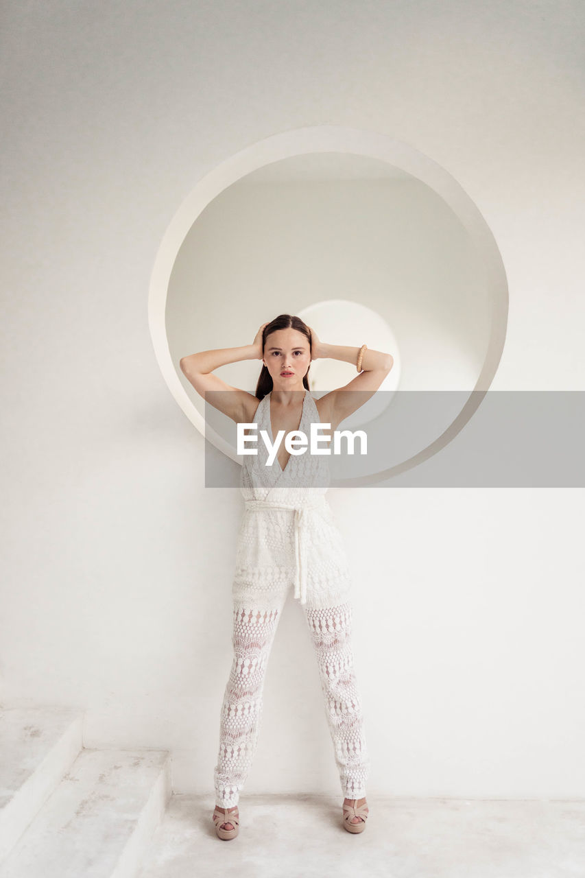 one person, white, indoors, full length, adult, women, standing, studio shot, young adult, front view, portrait, clothing, arms raised, toy, arm, holding, female, circle, smiling, pink, geometric shape, brown hair, casual clothing, emotion, looking at camera, photo shoot, happiness, person