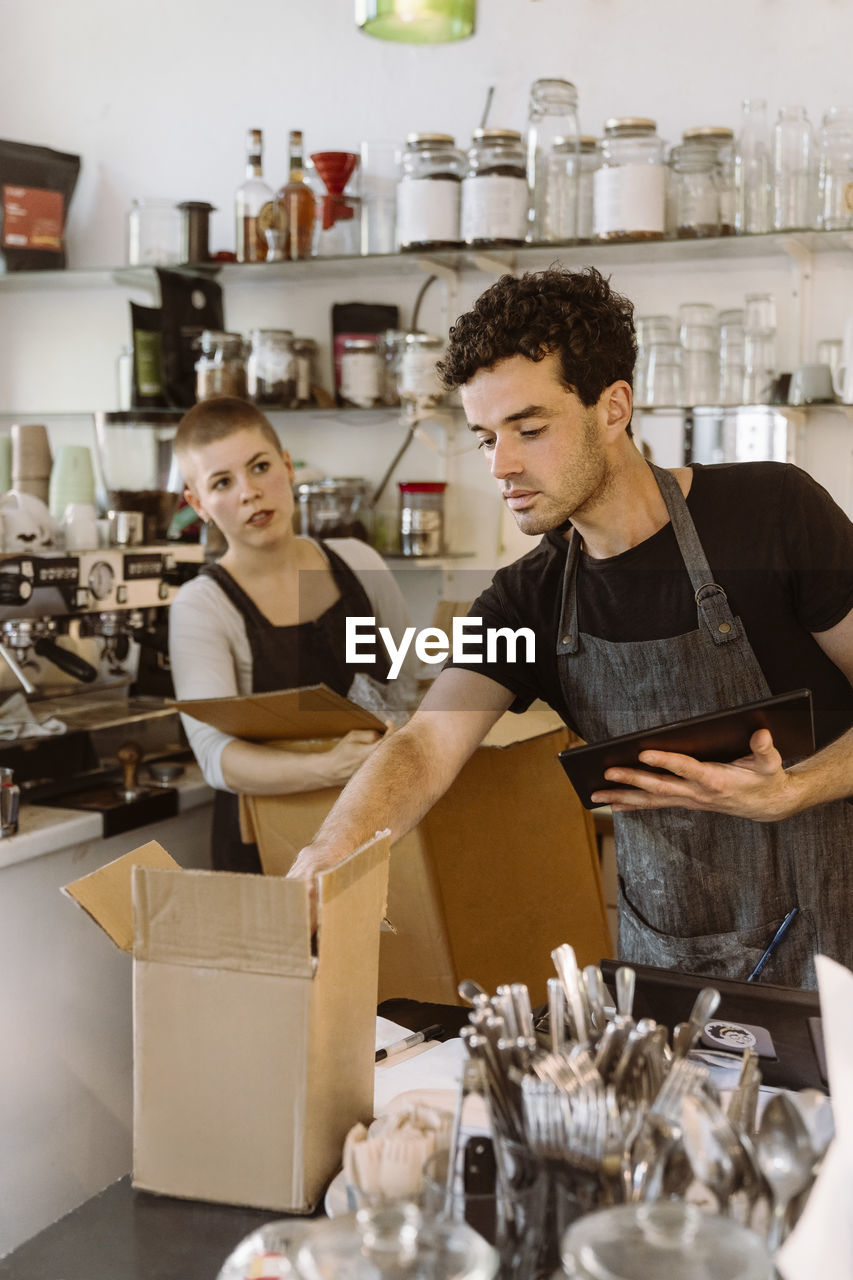 Male owner checking inventory with female colleague holding box in background