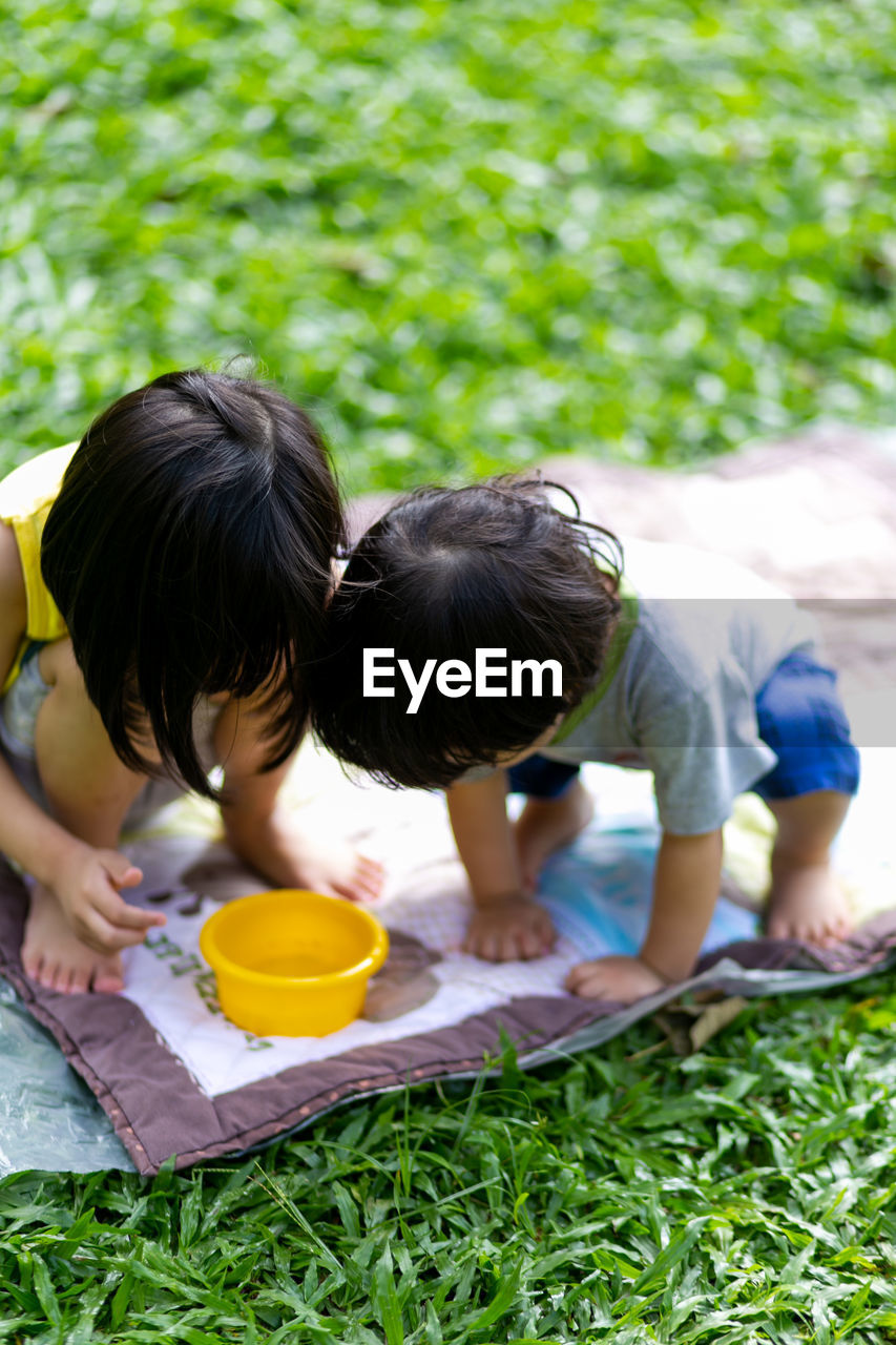 Children looking at container while crouching in public park