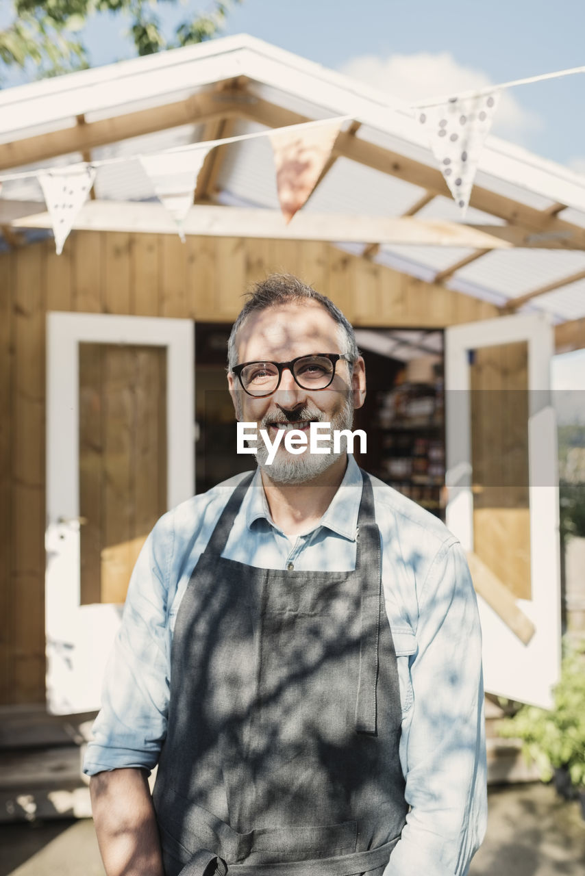 Portrait of happy mature store owner standing against shop