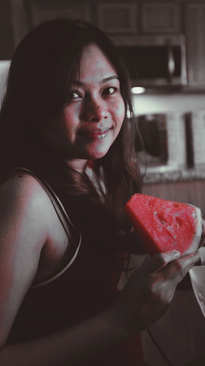 Portrait of smiling young woman holding watermelon slice at home