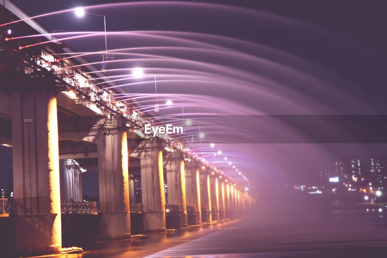 ILLUMINATED LIGHTS ON BRIDGE OVER CITY AT NIGHT