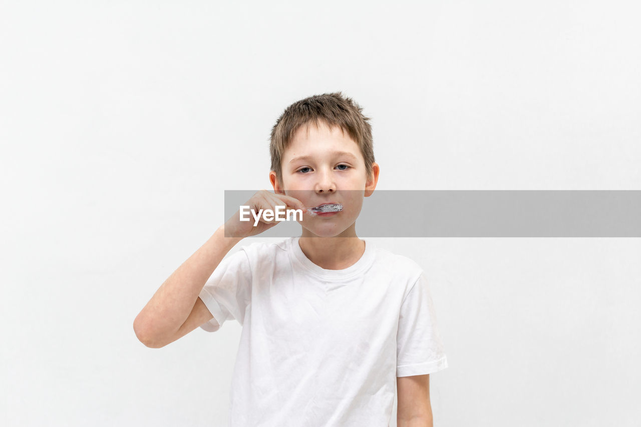 A boy in a white t-shirt is brushing his teeth in the bathroom.