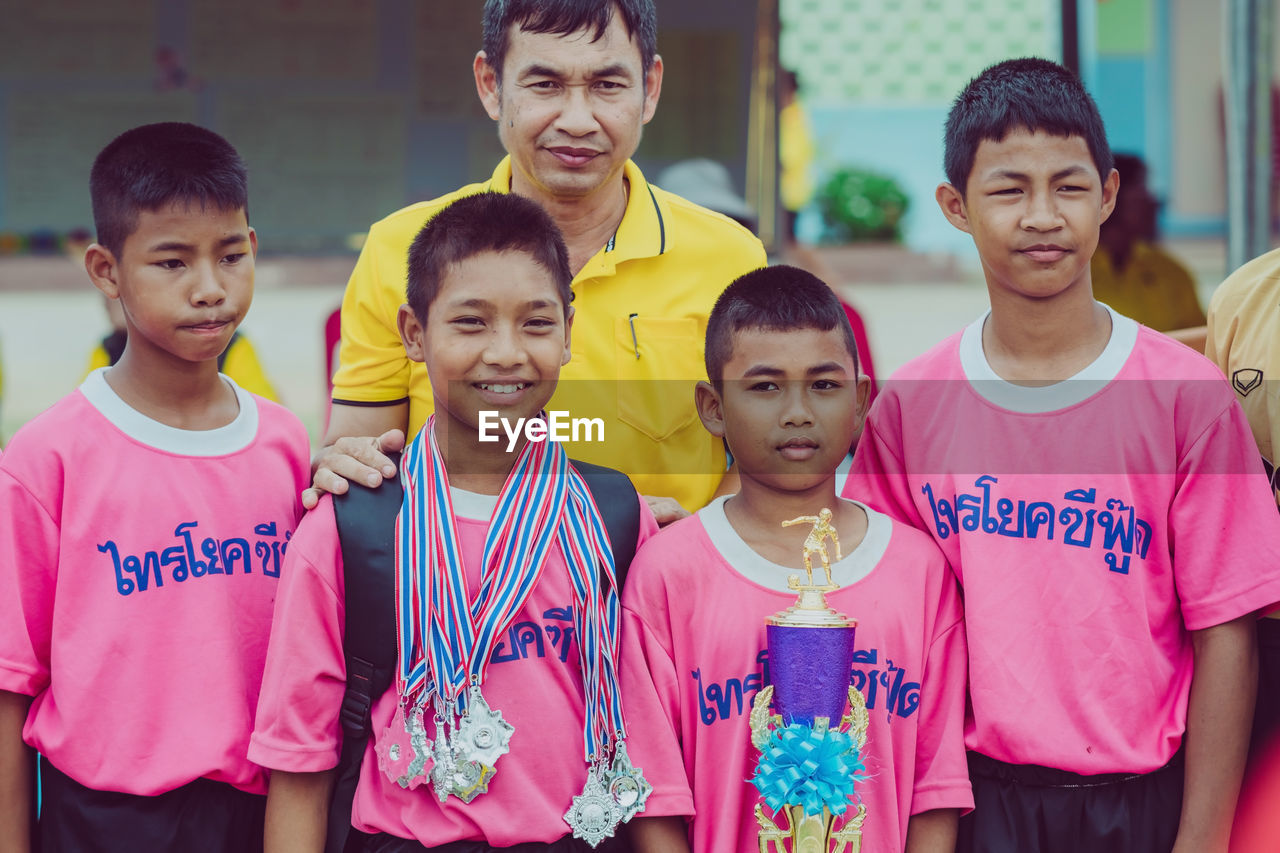 PORTRAIT OF A SMILING BOY WITH PEOPLE IN THE BACKGROUND