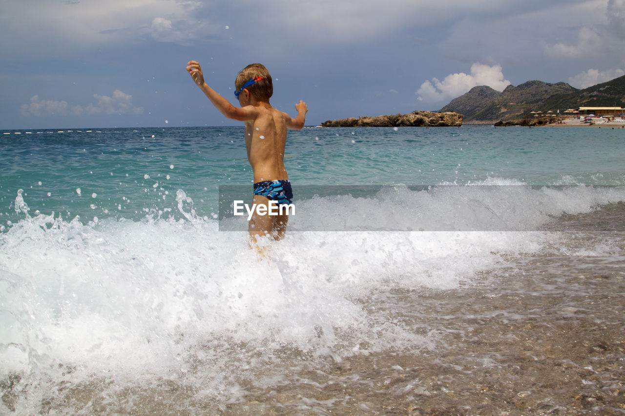 Full length of shirtless man in sea against sky