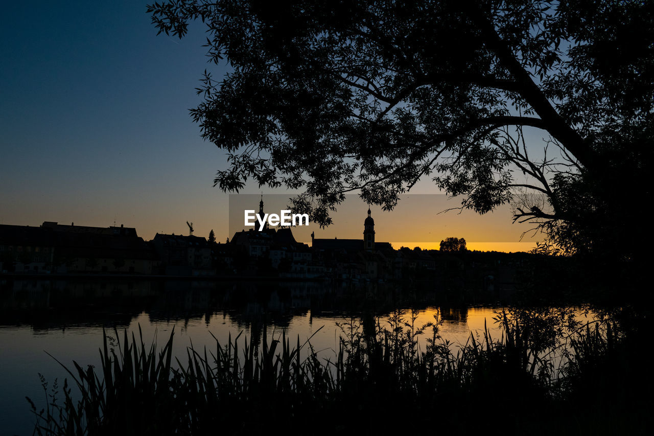 Silhouette trees by lake against sky during sunset