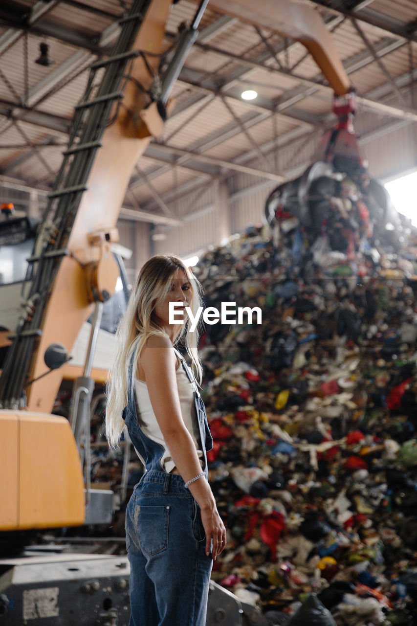 Portrait of young woman standing against garbage heap