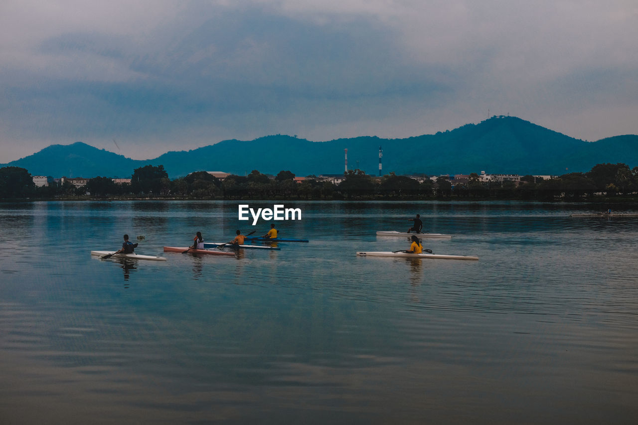 People rowing in lake against sky