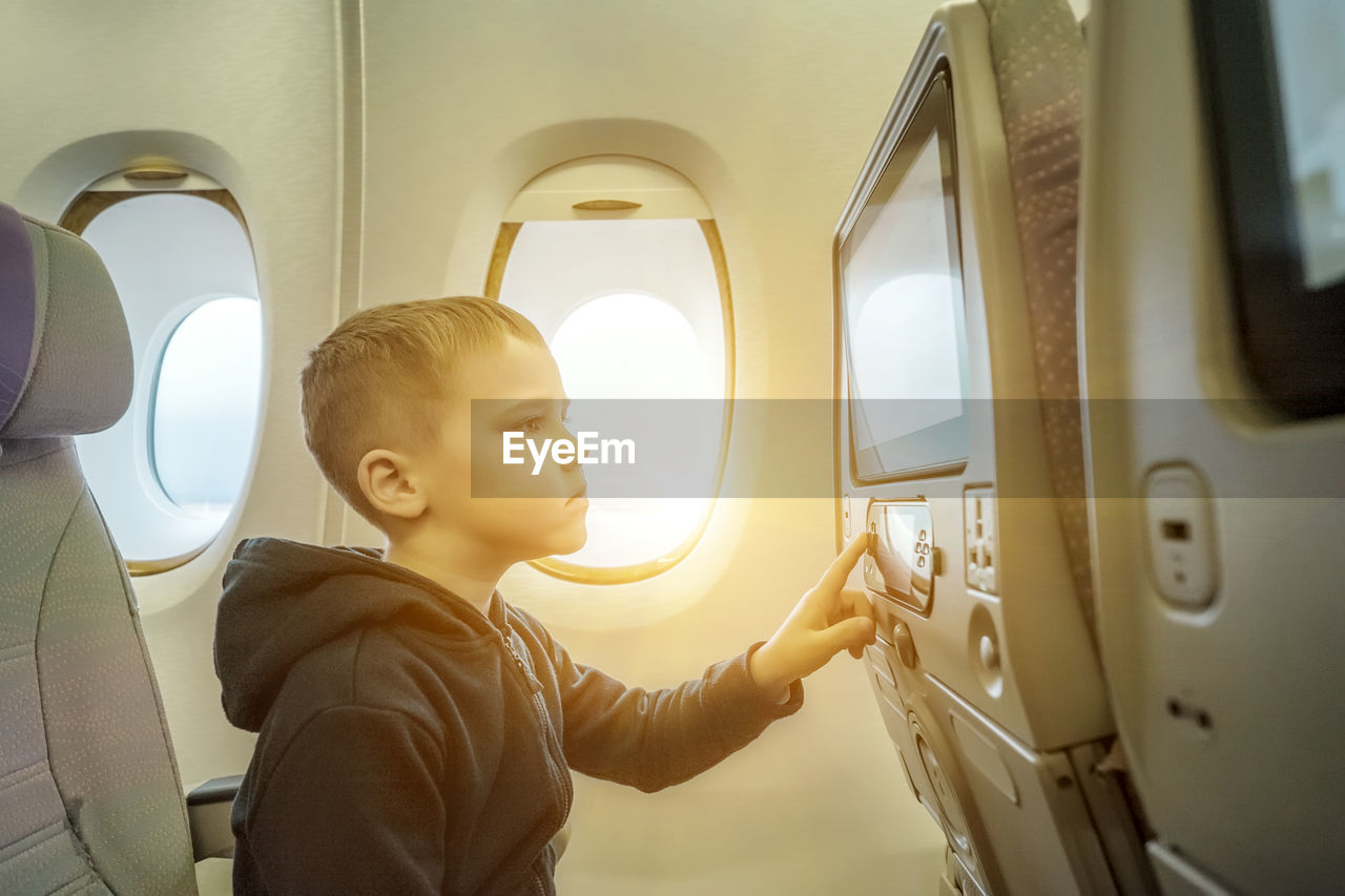 Little boy traveling by airplane. child sitting by aircraft window and looking on monitor. traveling