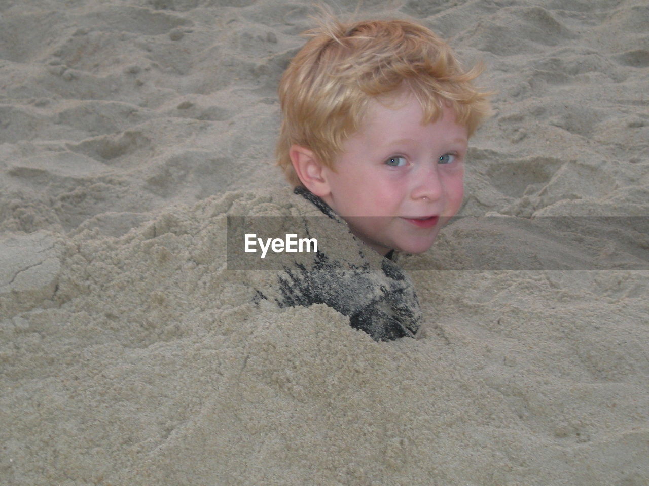 Portrait of playful boy covered with sand at beach