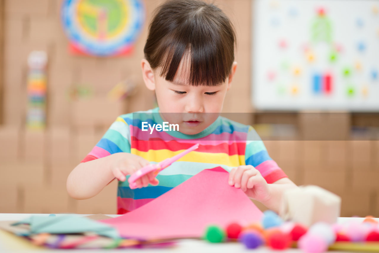 Young girl using scissors cutting papper for making craft for homeschooling