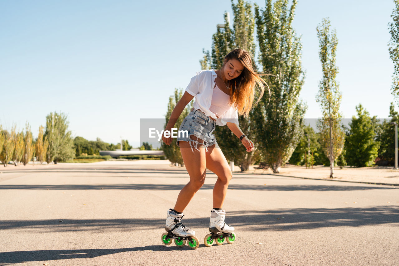 Side view of fit female in rollerblades showing stunt on road in city in summer