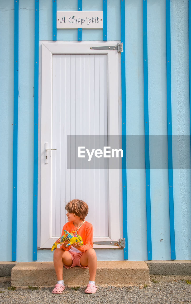 FULL LENGTH OF BOY SITTING ON BLUE CHAIR