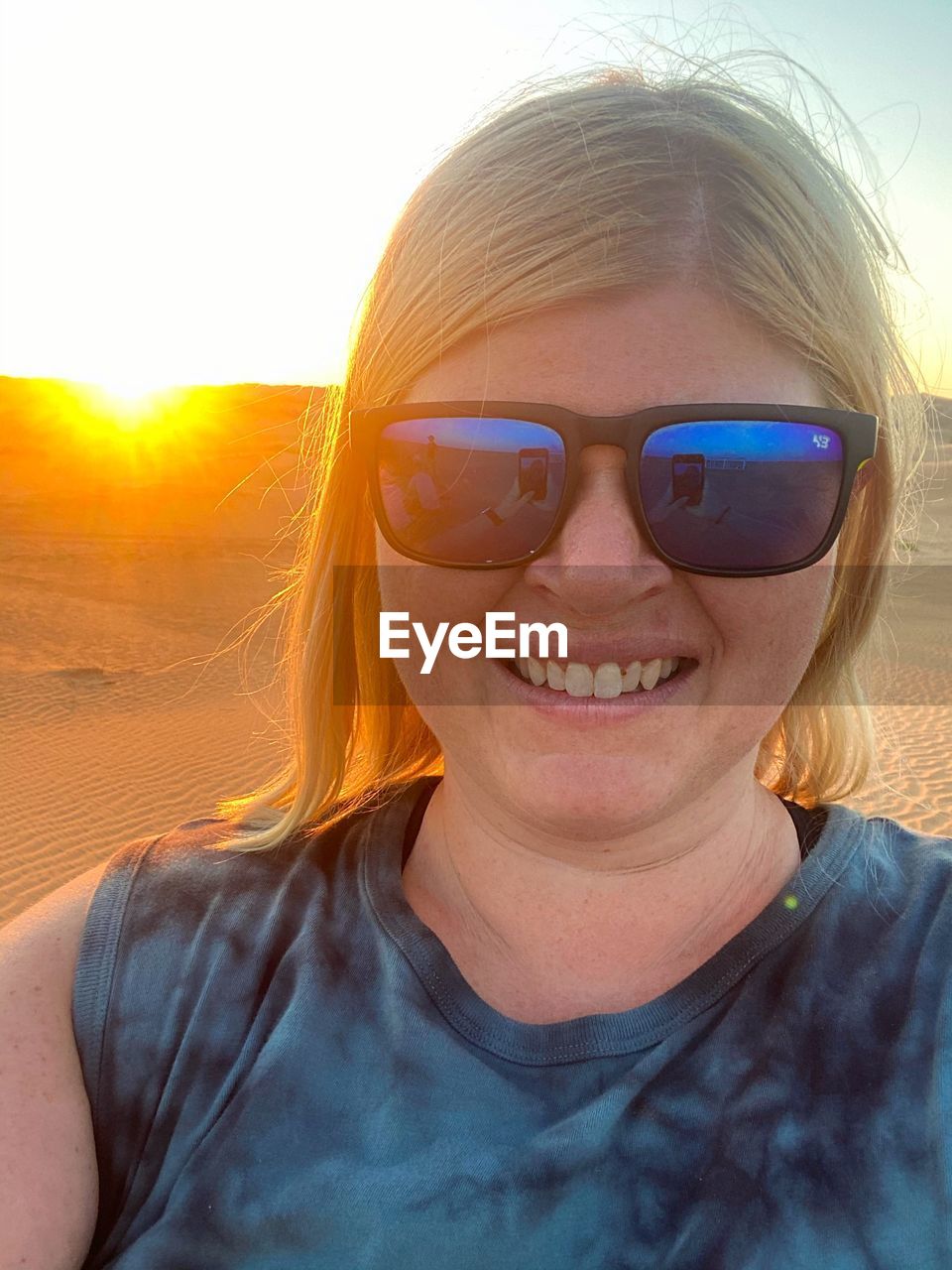 Portrait of smiling young woman wearing sunglasses in desert at sunset 