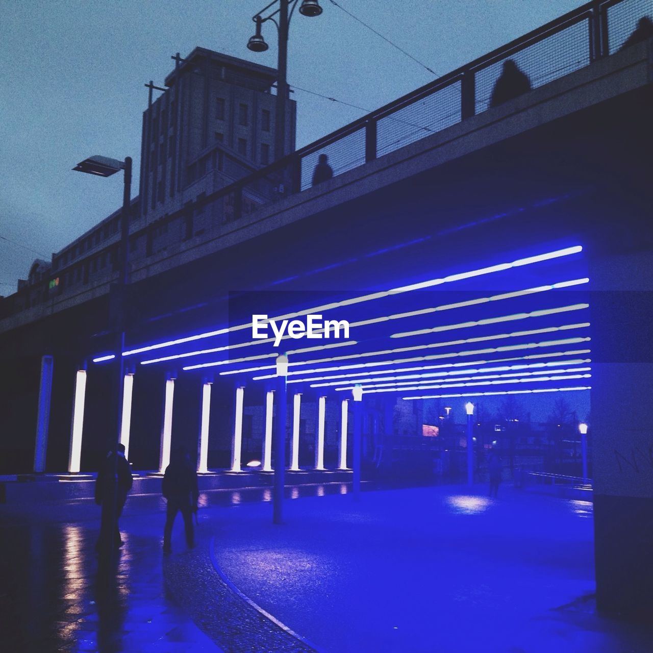 Illuminated blue light fixtures below bridge in city