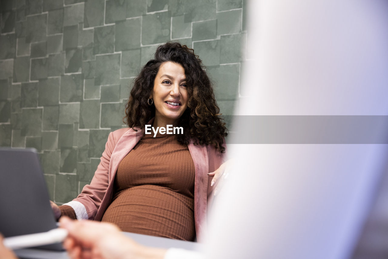 Smiling pregnant businesswoman talking with female colleague in office