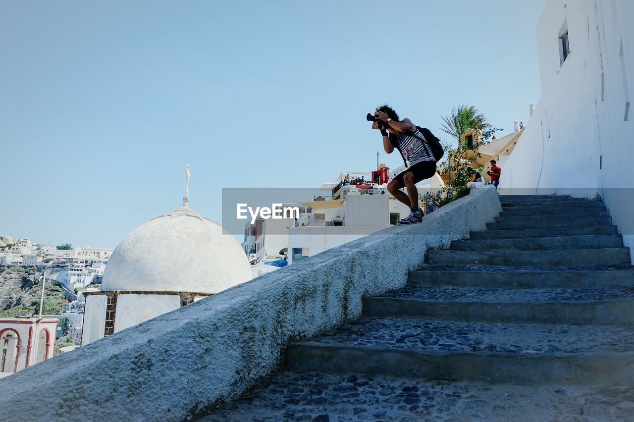 Low angle view of man photographing while standing on retaining wall