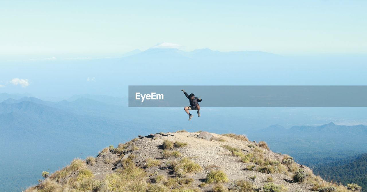 Happy mature man jumping on mountain against sky