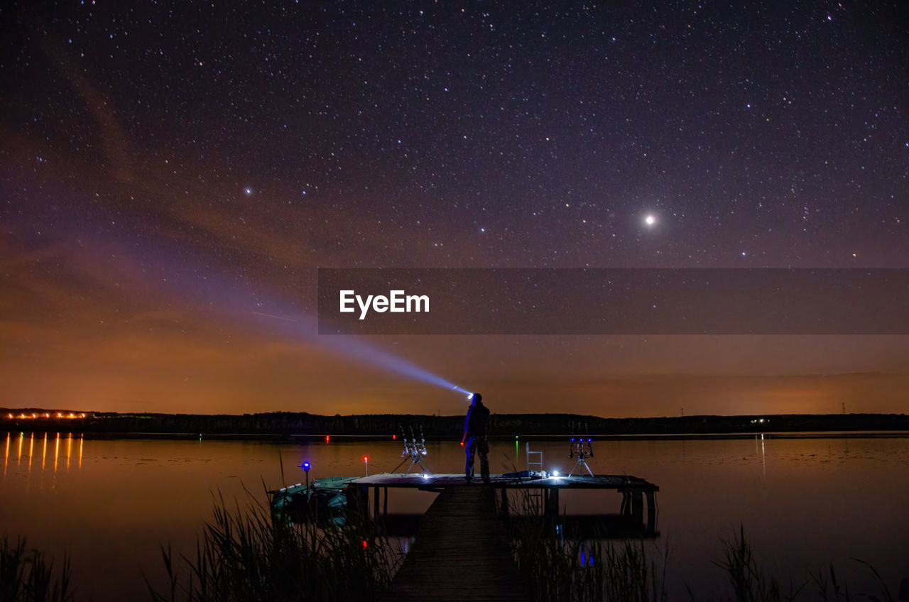 Full length of man holding flashlight by lake at night