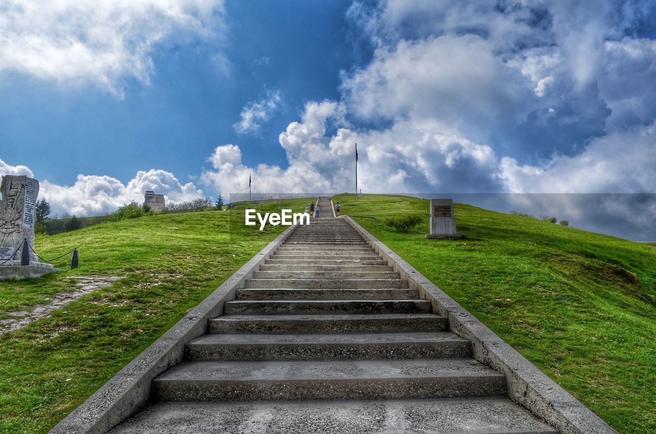 Staircase leading towards green landscape against sky