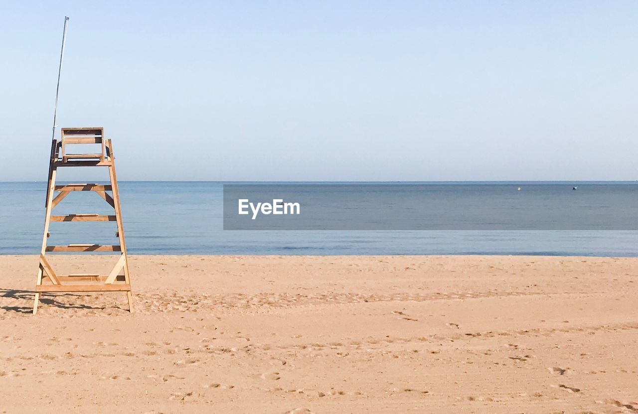 Lifeguard chair on sand at beach against clear sky