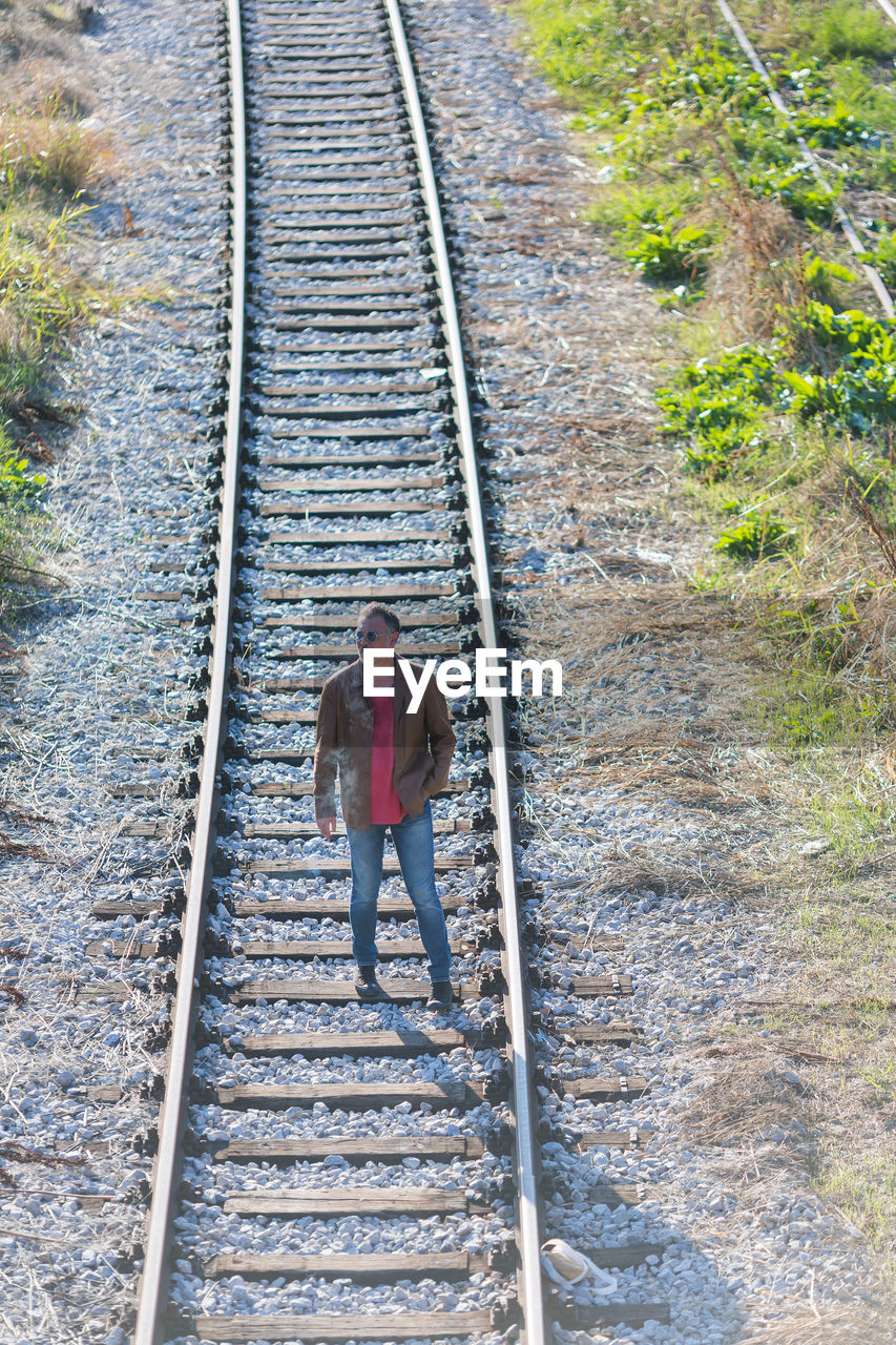 track, railroad track, rail transportation, transport, full length, one person, the way forward, high angle view, transportation, day, men, rolling stock, nature, adult, lifestyles, outdoors, walking, leisure activity, railway, diminishing perspective, travel, casual clothing, front view, standing, plant, vehicle, architecture