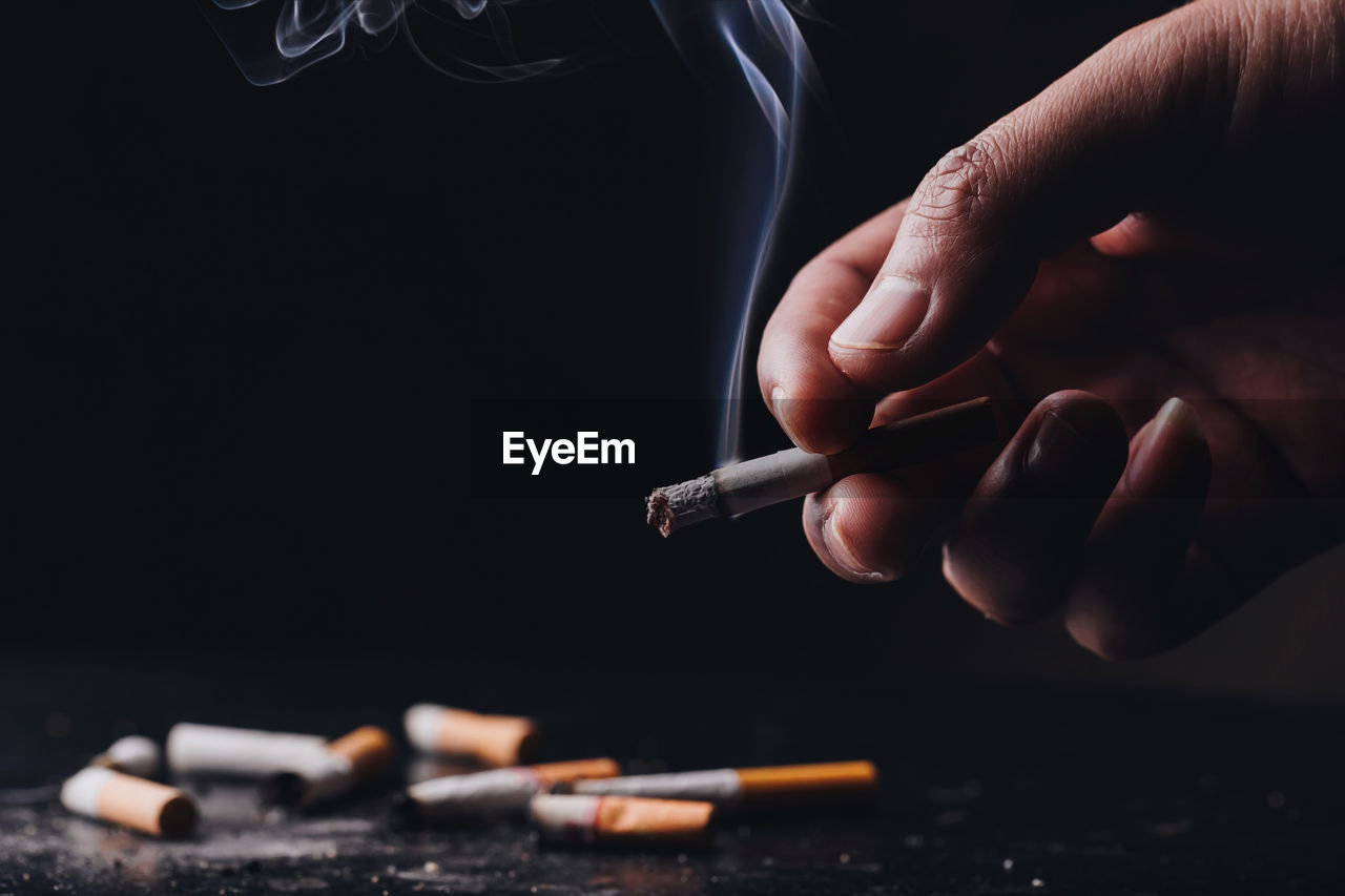 Cropped hand of person holding cigarette against black background
