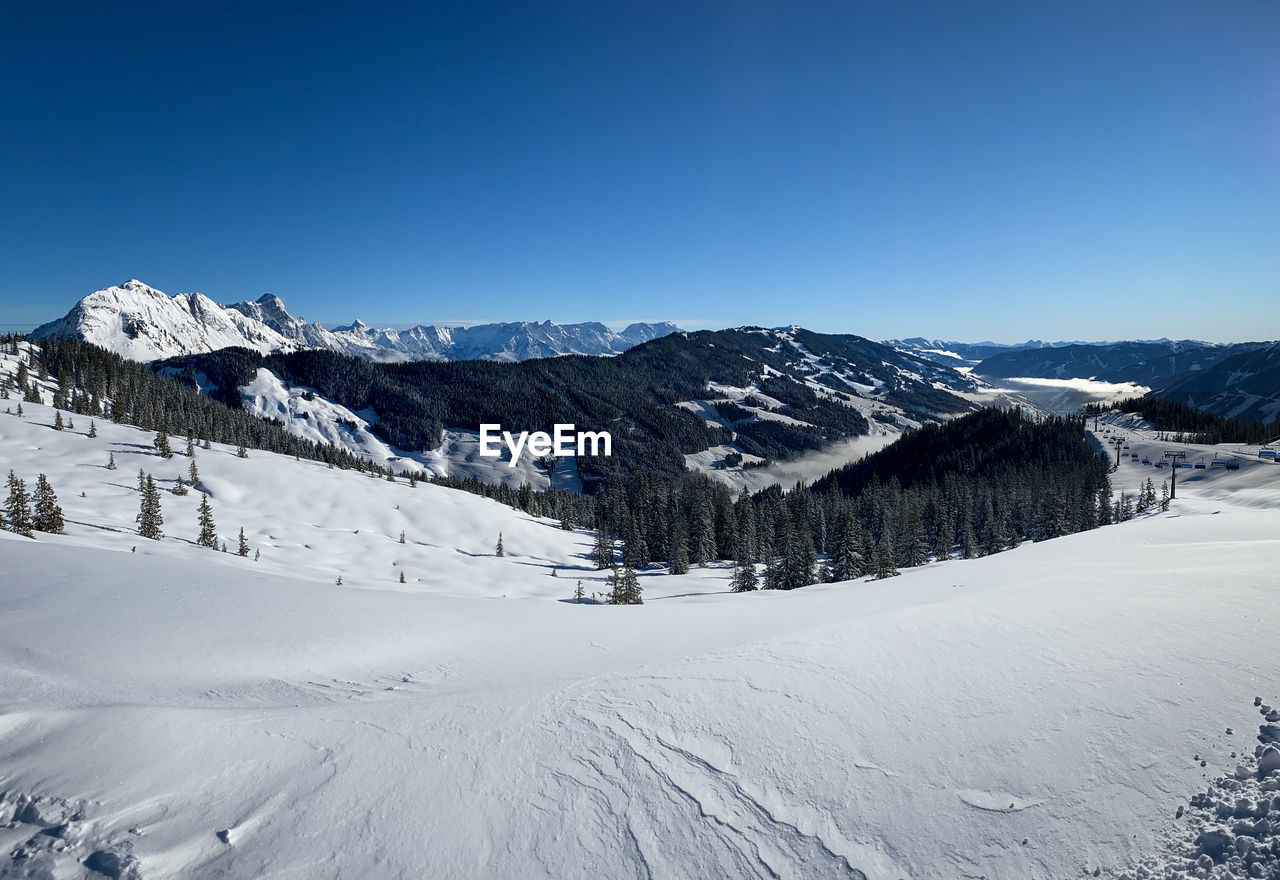 Scenic view of snow covered mountains in saalbach hinterglemm in the austrian alps against blue sky