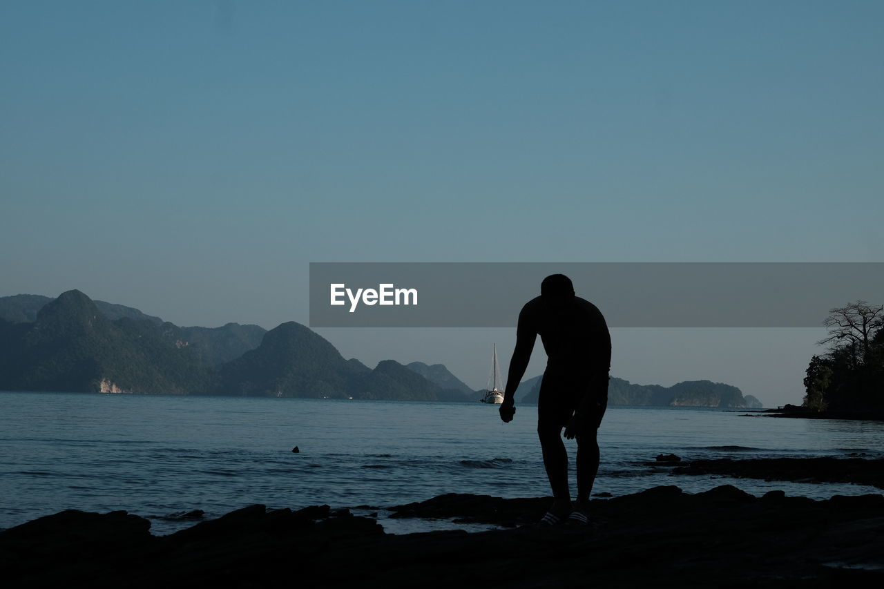 Silhouette man standing by lake against clear sky