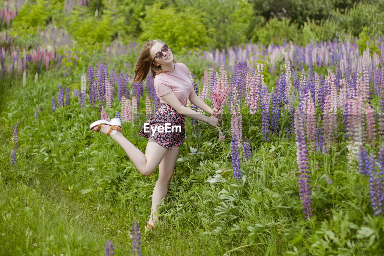 Young woman in the field of flowers with bunch of lupines dancing