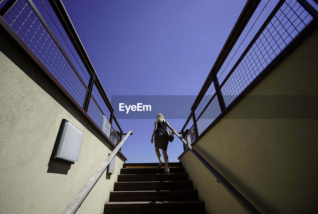 Rear view of woman moving up stairs against clear blue sky