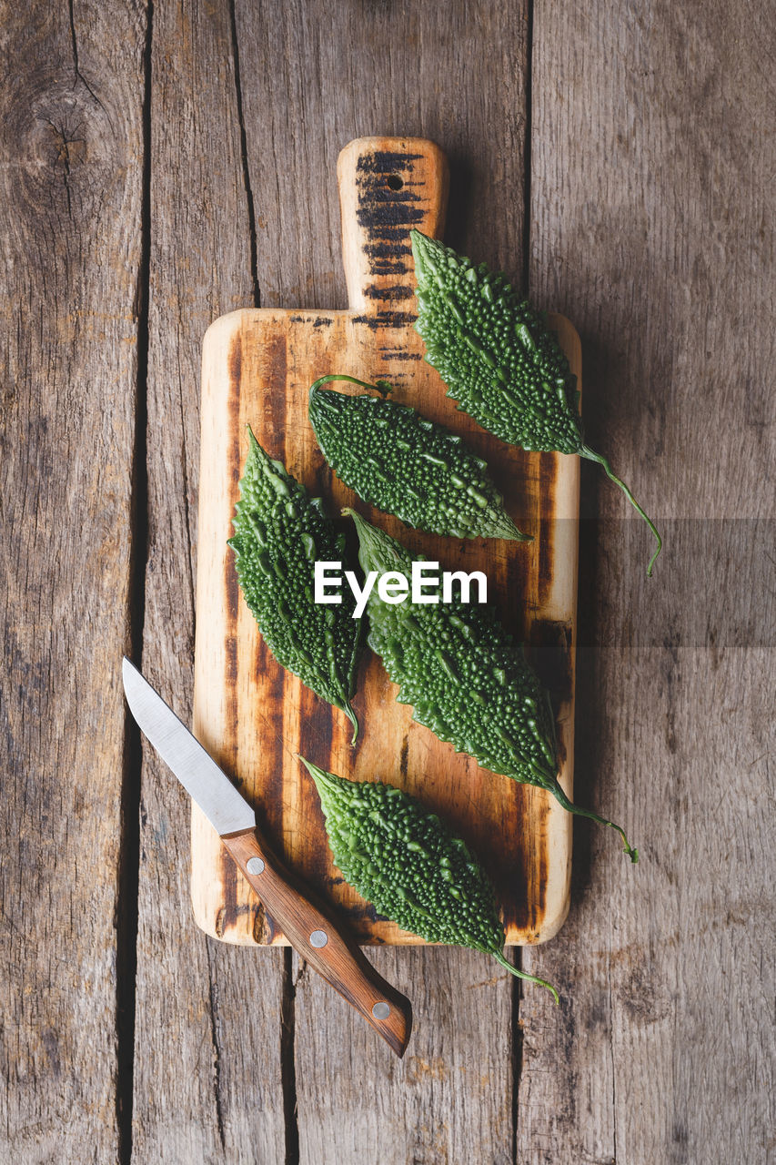 High angle view of bitter gourds with cutting board on wooden table