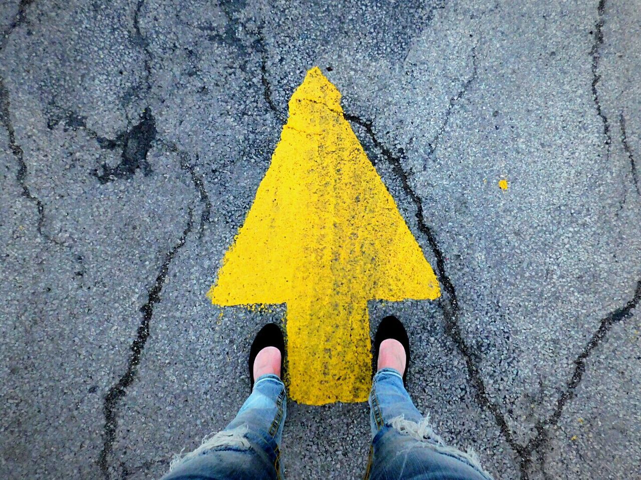 Low section of woman standing on yellow arrow symbol at road
