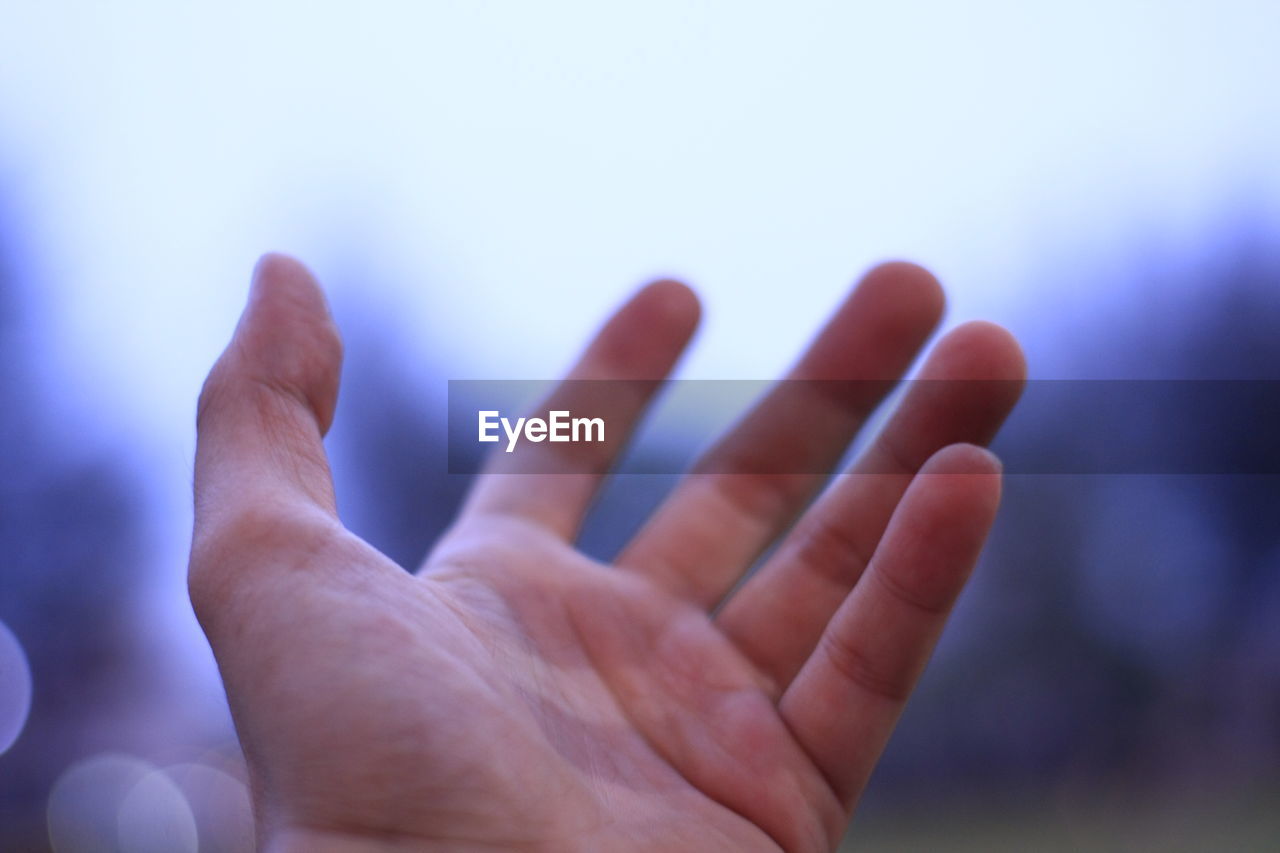 Close-up of human hand gesturing against sky