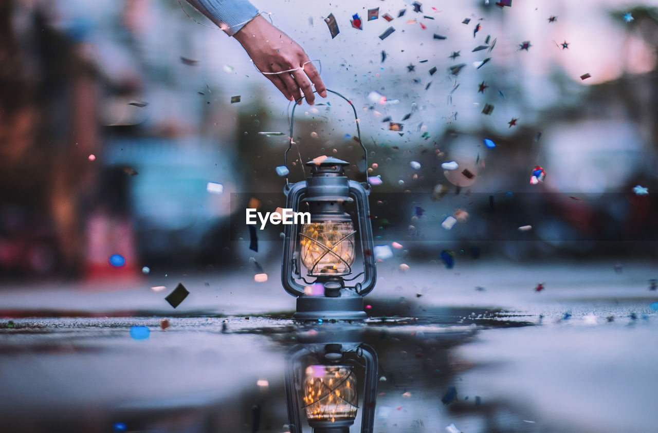 Cropped image of hand picking up illuminated lantern with string lights by confetti on street