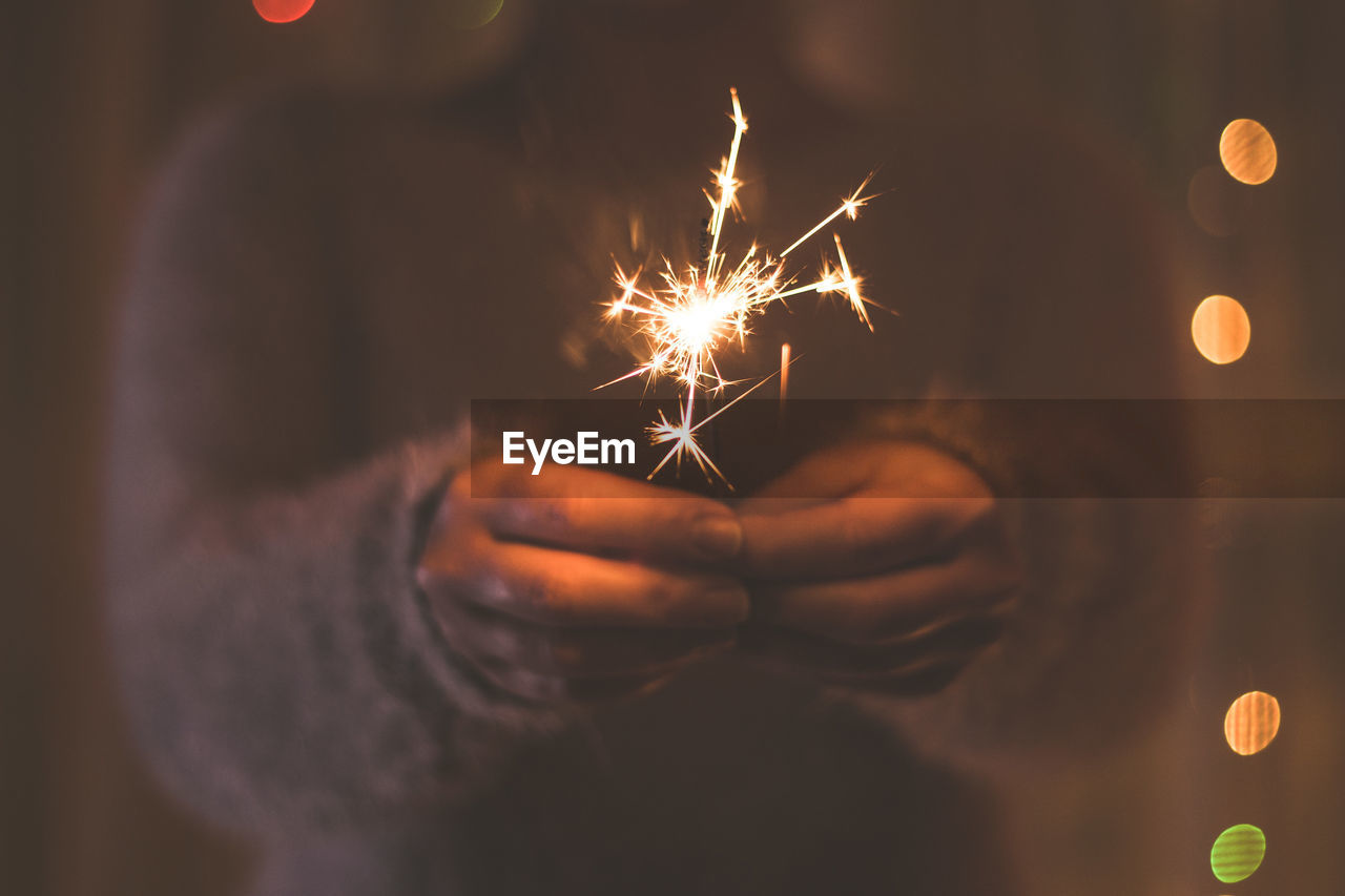 Midsection of woman holding lit sparkler at night