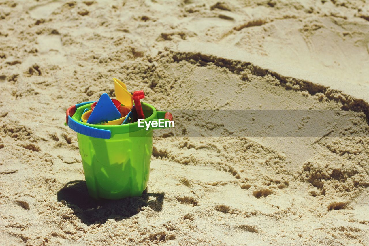 High angle view of bucket with toys on sand at beach