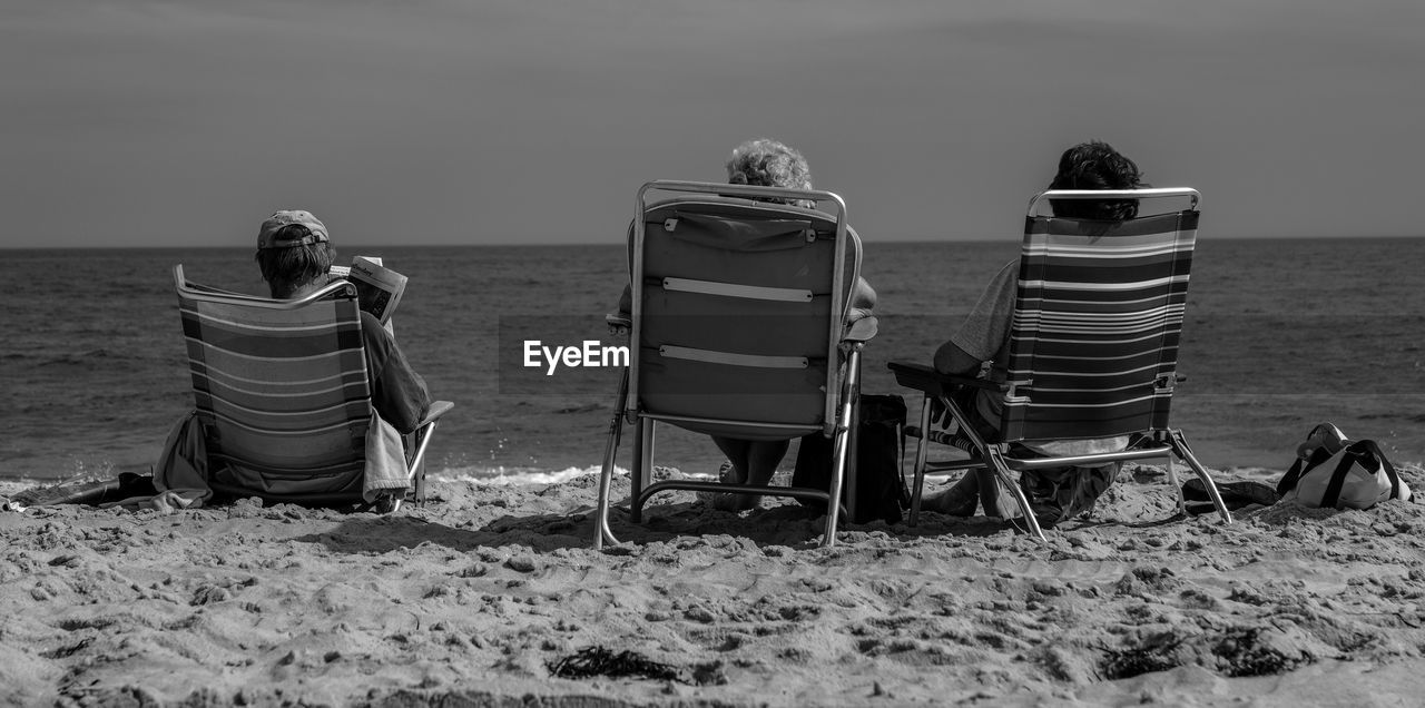 Rear view of people sitting on chairs at beach