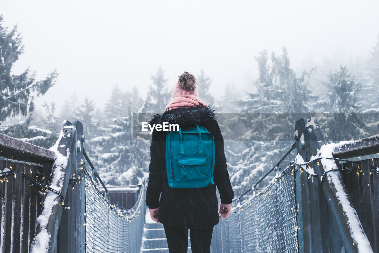 Rear view of woman standing on footbridge during winter