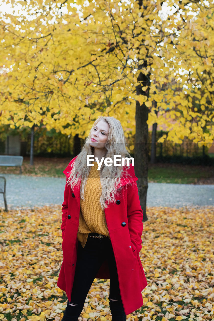 Young woman looking away while standing at park during autumn