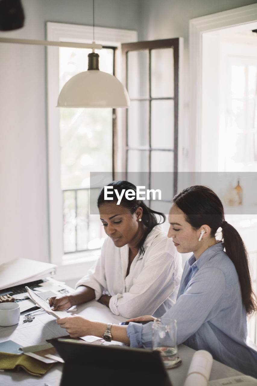 Side view of architect discussing with coworker while working at table in home office